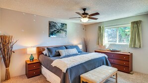 A bedroom with a bed, bedside tables, a bench, a ceiling fan, a window with curtains, and a wall painting. - Pet-friendly 55+ Green Valley Home w/ Golf Gear! (Green Valley)