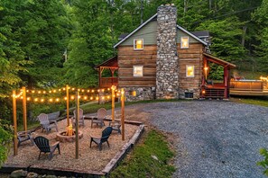 Une cabane en rondins avec une cheminée en pierre, un espace salon extérieur et des guirlandes lumineuses.