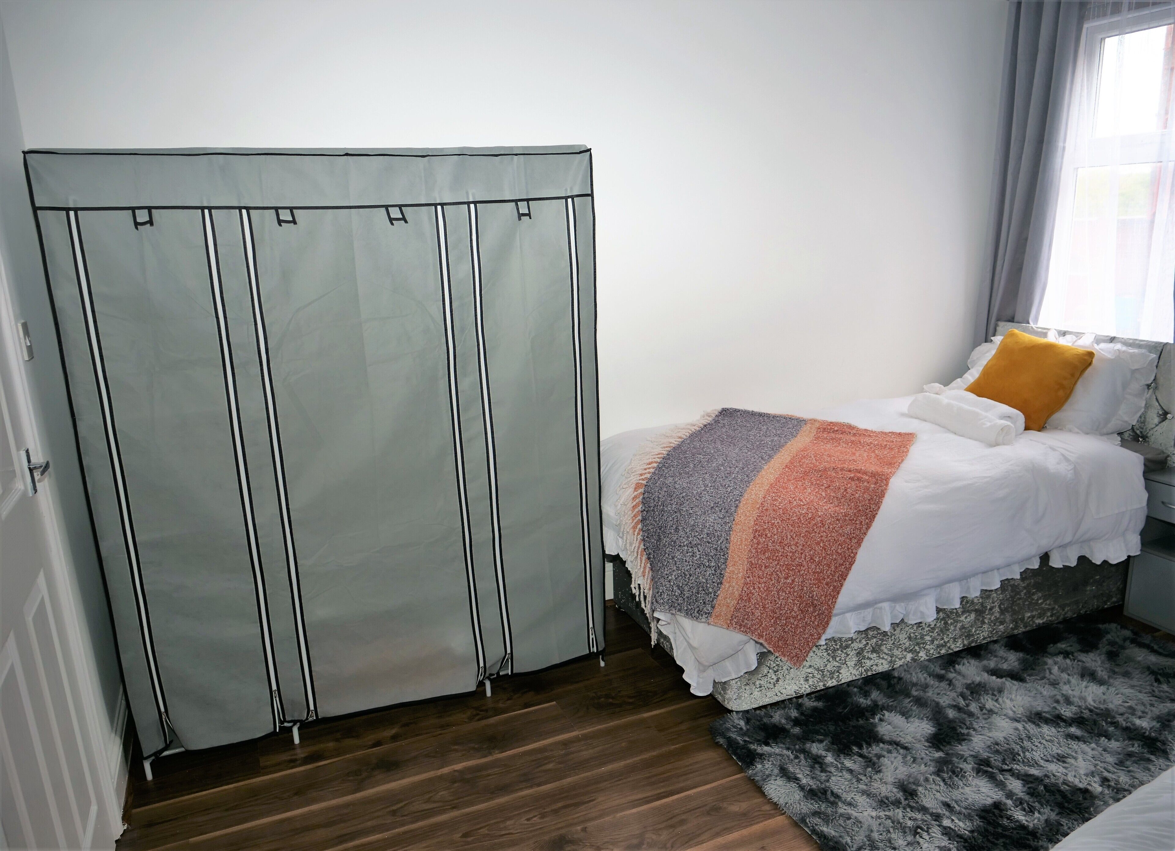 Ein Schlafzimmer mit einem Bett, einem grauen Kleiderschrank, einem schwarz-weißen Teppich und einem Fenster mit Vorhängen.