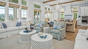 A spacious living room with a white sofa, patterned armchairs, and a dining area with a kitchen in the background. - Premier Lakefront Beach Home@Cinnamon Shore South By Luxe Pools & Amenities (Port Aransas)