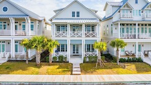 A beachfront property with multiple white buildings, a wooden deck, and palm trees. - Premier Lakefront Beach Home@Cinnamon Shore South By Luxe Pools & Amenities (Port Aransas)