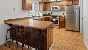 Eine Küche mit Holzschränken, einem Edelstahlkühlschrank, einer Mikrowelle und einer großen Kücheninsel mit Sitzgelegenheiten.