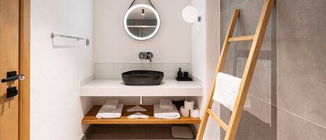A modern bathroom with a round mirror, a black sink, and a wooden ladder.