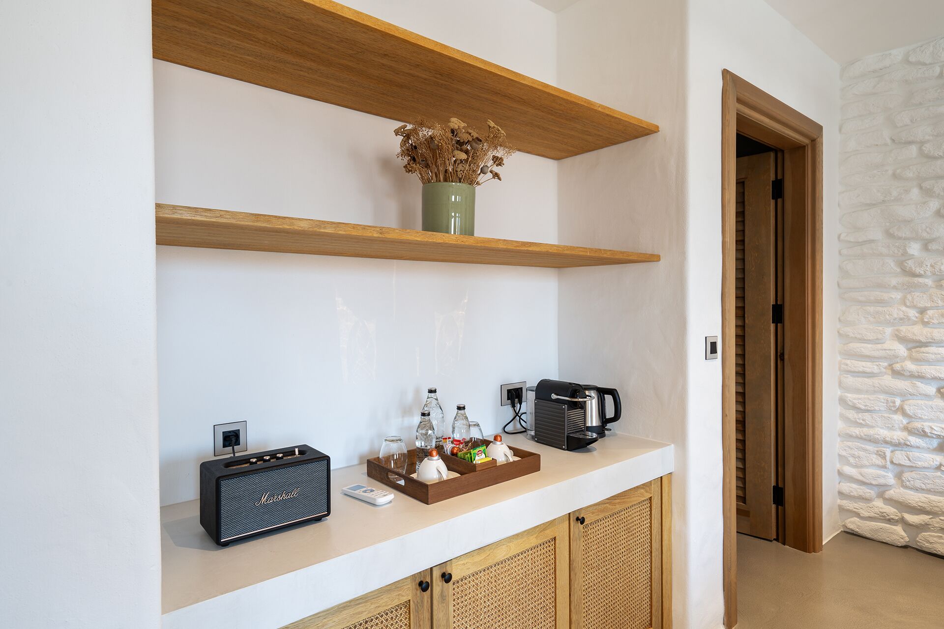 Een keukenhoek met een koffieapparaat, een radio en een vaas met gedroogde bloemen op een plank.