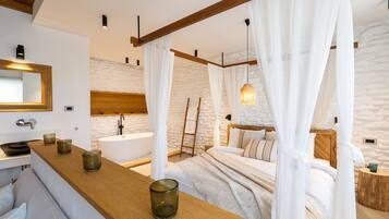 A bedroom with a large bed, a wooden headboard, a bedside table with candles, a nightstand, and a stone wall.