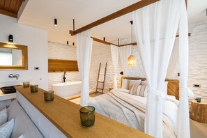 A bedroom with a large bed, a wooden headboard, a bedside table with candles, a nightstand, and a stone wall. - Nomad Hotel Side - Adults Only (Manavgat)