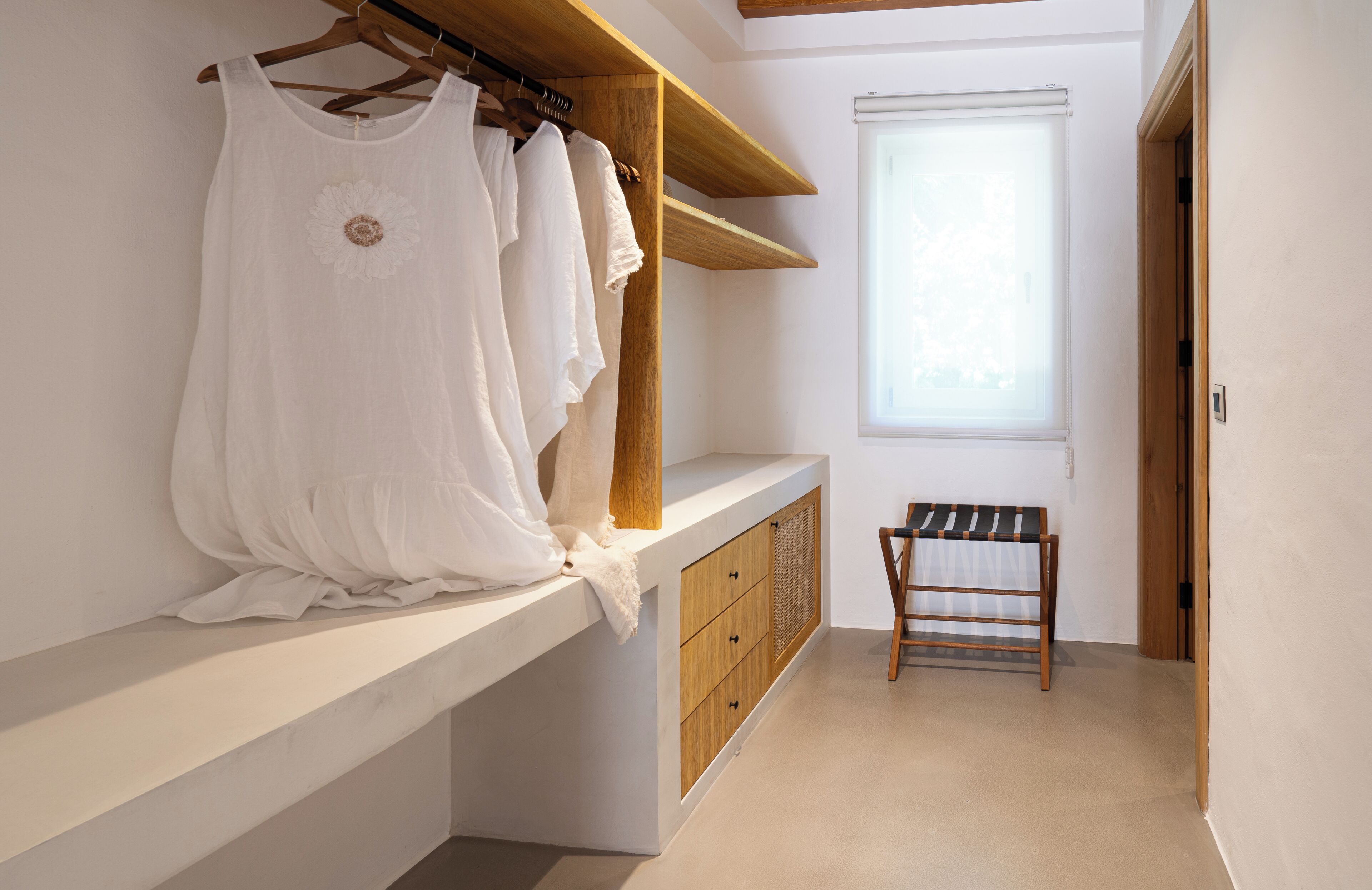Ein begehbarer Kleiderschrank mit einer Sitzbank, Holzregalen und hängender Kleidung.