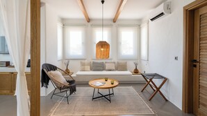 Una habitación acogedora con techo de madera, una mesa redonda con una revista, una silla de mimbre y un banco con cojines.