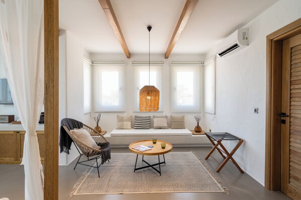 Una habitación acogedora con techo de madera, una mesa redonda con una revista, una silla de mimbre y un banco con cojines.