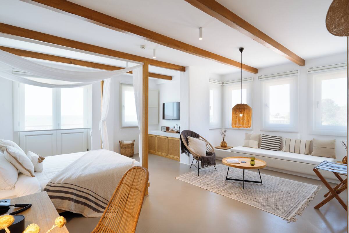 A modern hotel room with a bed, a sofa, a dining table, and a TV.