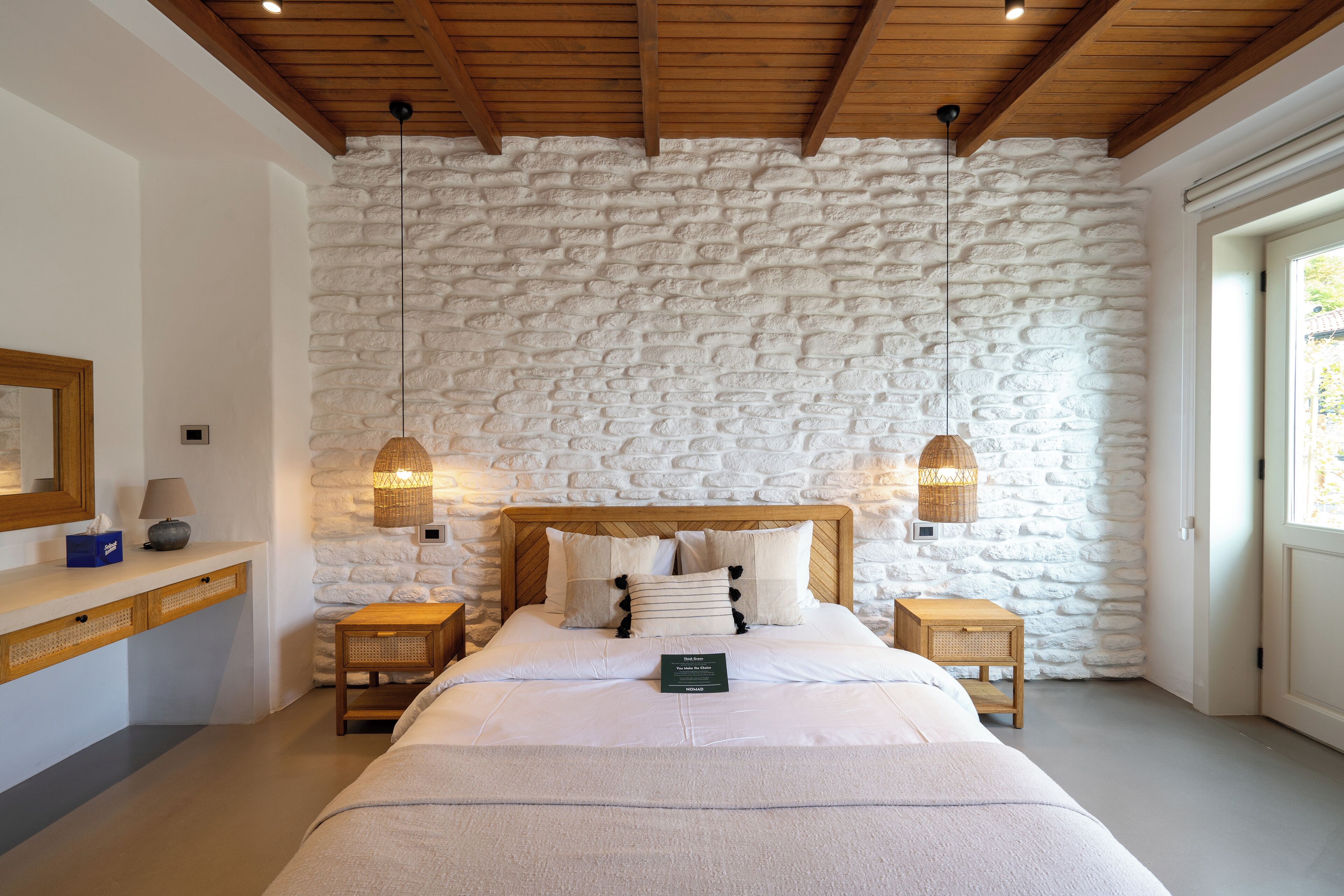 Une chambre avec un mur en pierre, des poutres en bois au plafond, un lit avec une literie blanche, deux tables de chevet avec des lampes et une petite table de nuit avec une lampe.