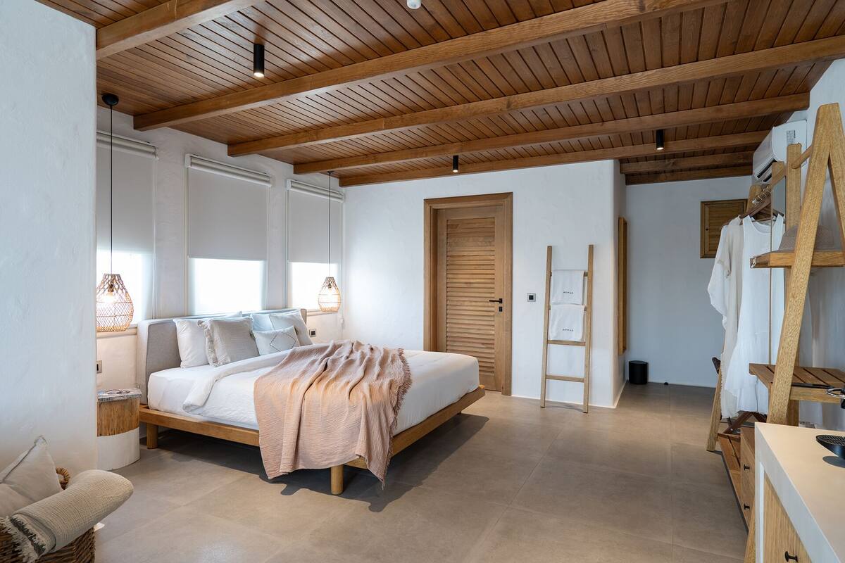 A bedroom with a wooden ceiling, a bed with a beige blanket, a wooden wardrobe, and a ladder.
