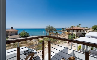 Un balcón con vistas al mar, un coche blanco y una pérgola de madera con mobiliario para exteriores.