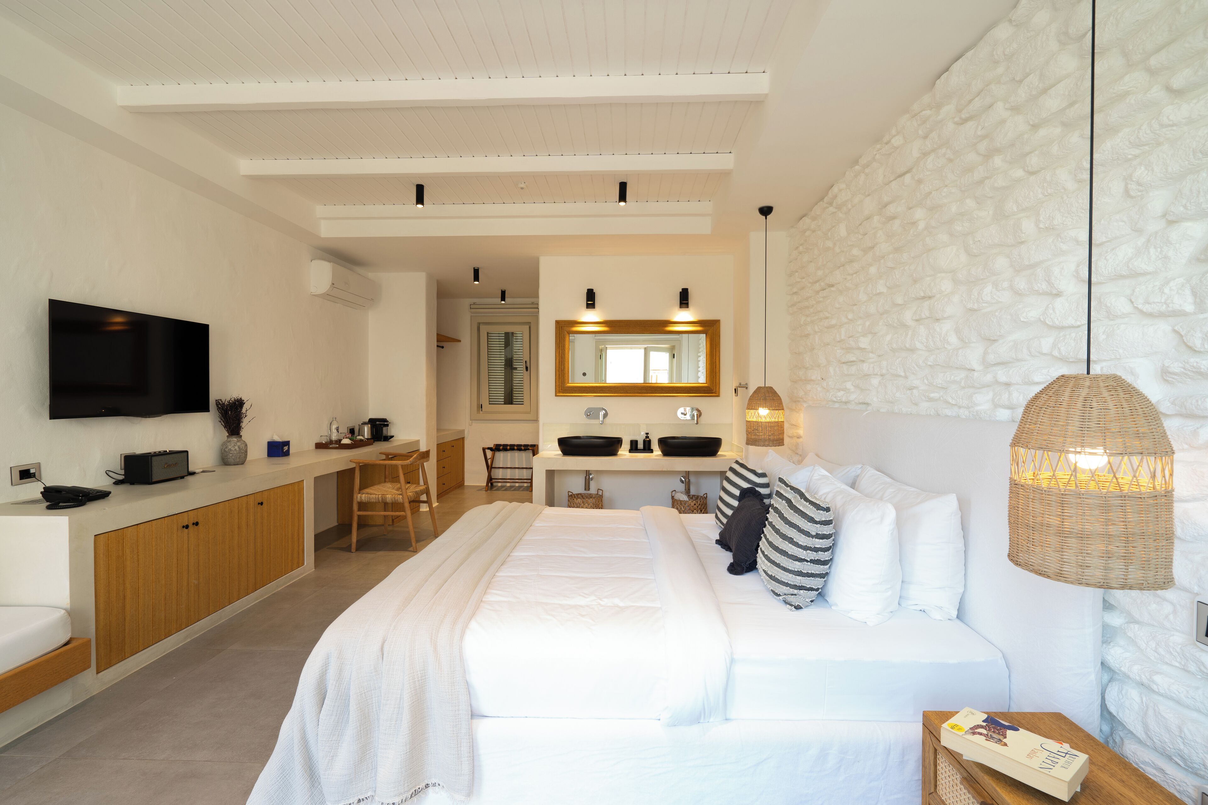 Un dormitorio moderno con una cama grande, una mesita de noche, un televisor, un área de cocina y un baño con espejo y lavamanos.