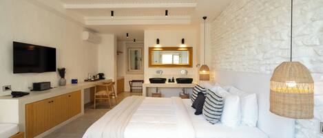 Un dormitorio moderno con una cama grande, una mesita de noche, un televisor, un área de cocina y un baño con espejo y lavamanos.