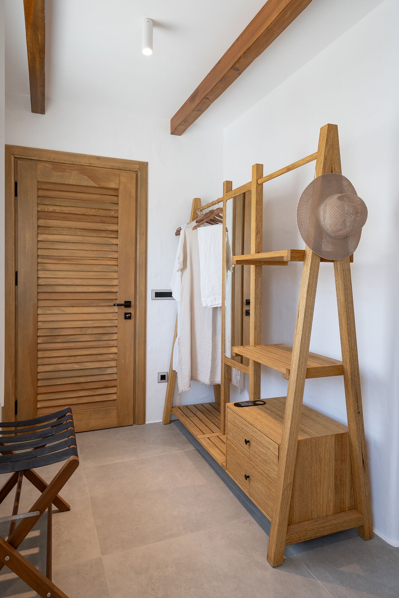 A wooden wardrobe with shelves and a hanging rack, a wooden chair, and a door with horizontal slats.