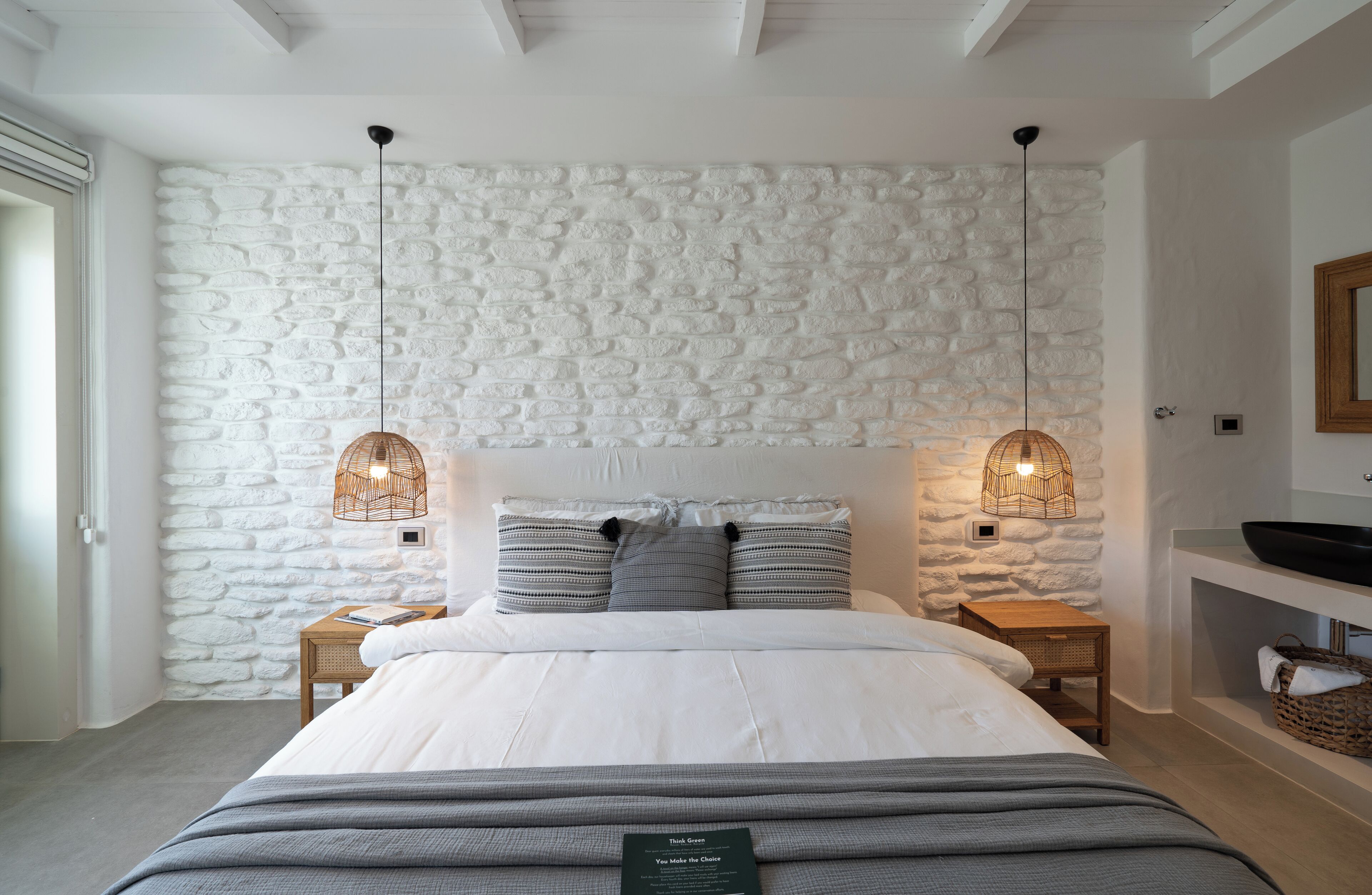 Ein Schlafzimmer mit einer Steinsandsteinwand, einem Bett mit grauer Bettwäsche, zwei Nachttischen mit Weidenlampen und einem Nachttischregal.