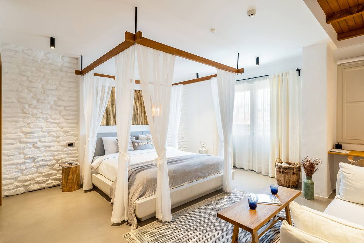 A bedroom with a four-poster bed, a stone wall, a wooden ceiling, and a view of the outdoors.
