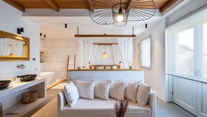 Una sala de estar moderna con un sofá blanco, techo de madera, pared de piedra, ventana grande y lámpara colgante.