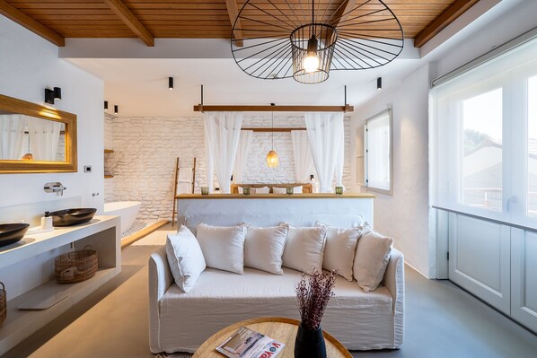 Un salon moderne avec un canapé blanc, un plafond en bois, un mur en pierre, une grande fenêtre et un luminaire suspendu.
