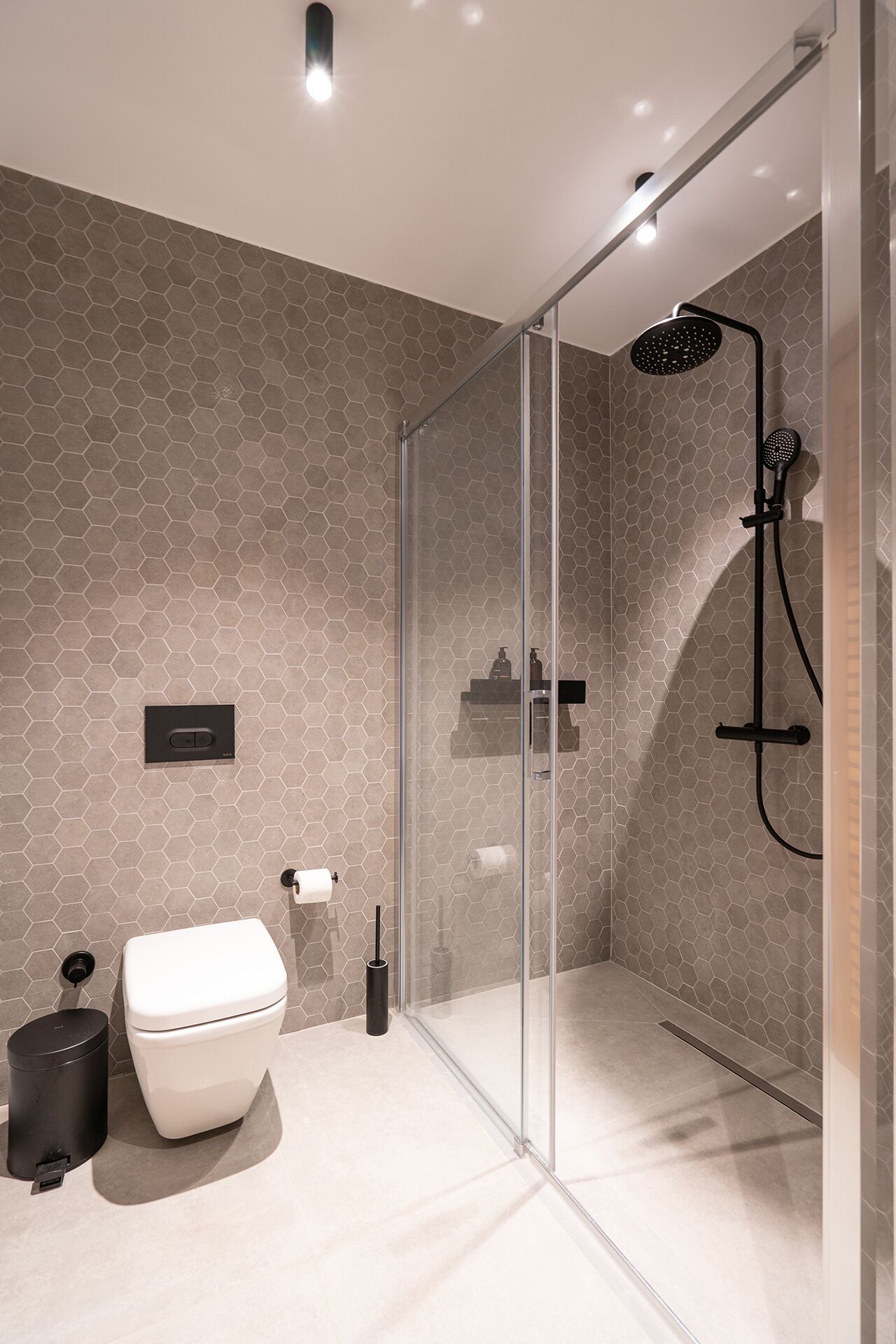 A modern bathroom with a glass shower enclosure, a toilet, and a trash can.