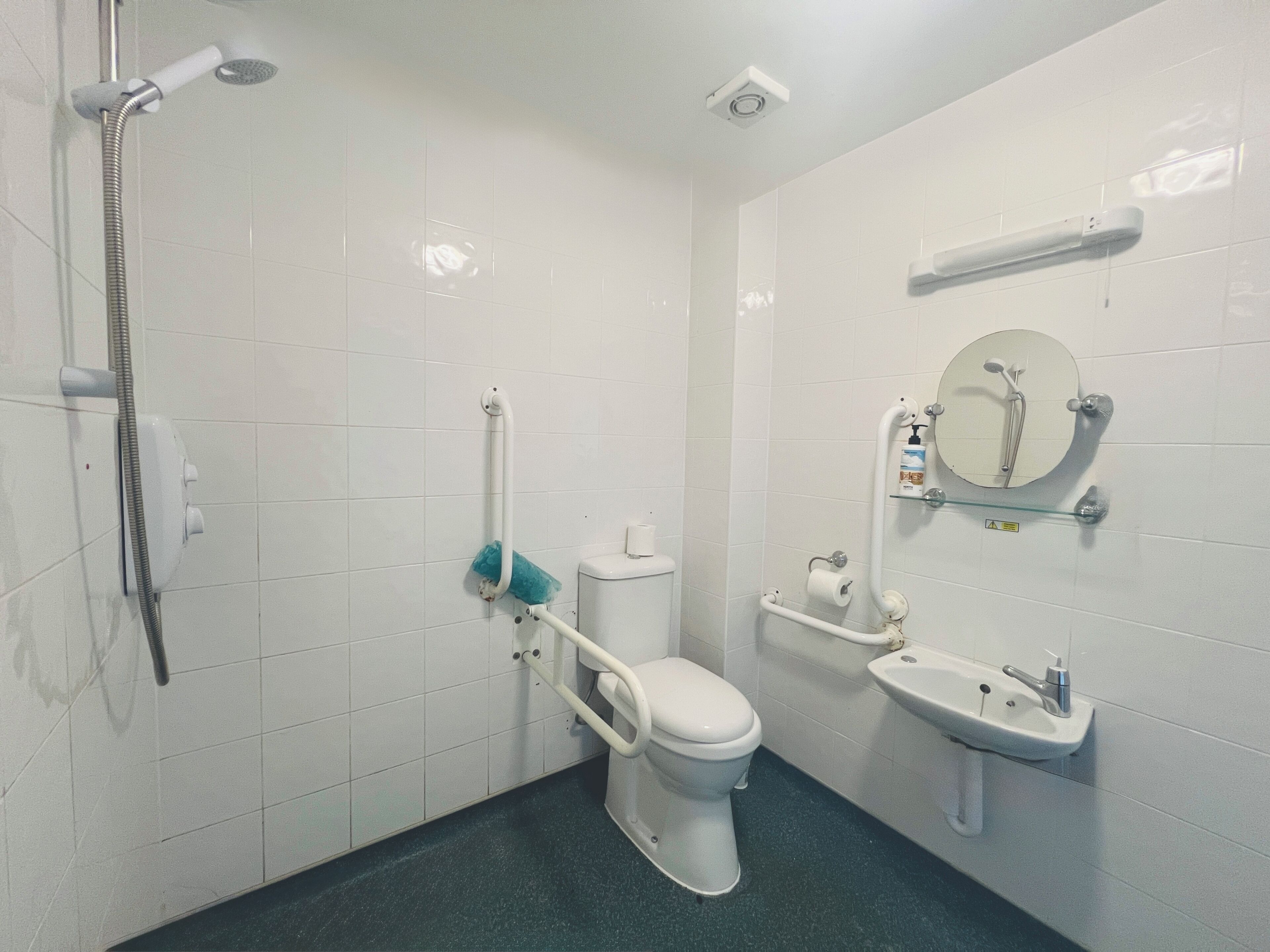 A bathroom with a toilet, sink, shower, and grab bars.
