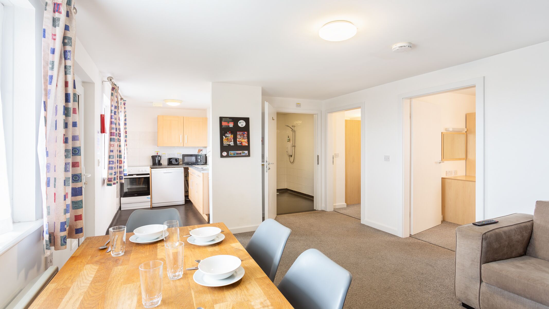 A modern apartment with a dining area, kitchenette, shower, and a living room with a sofa and remote control.