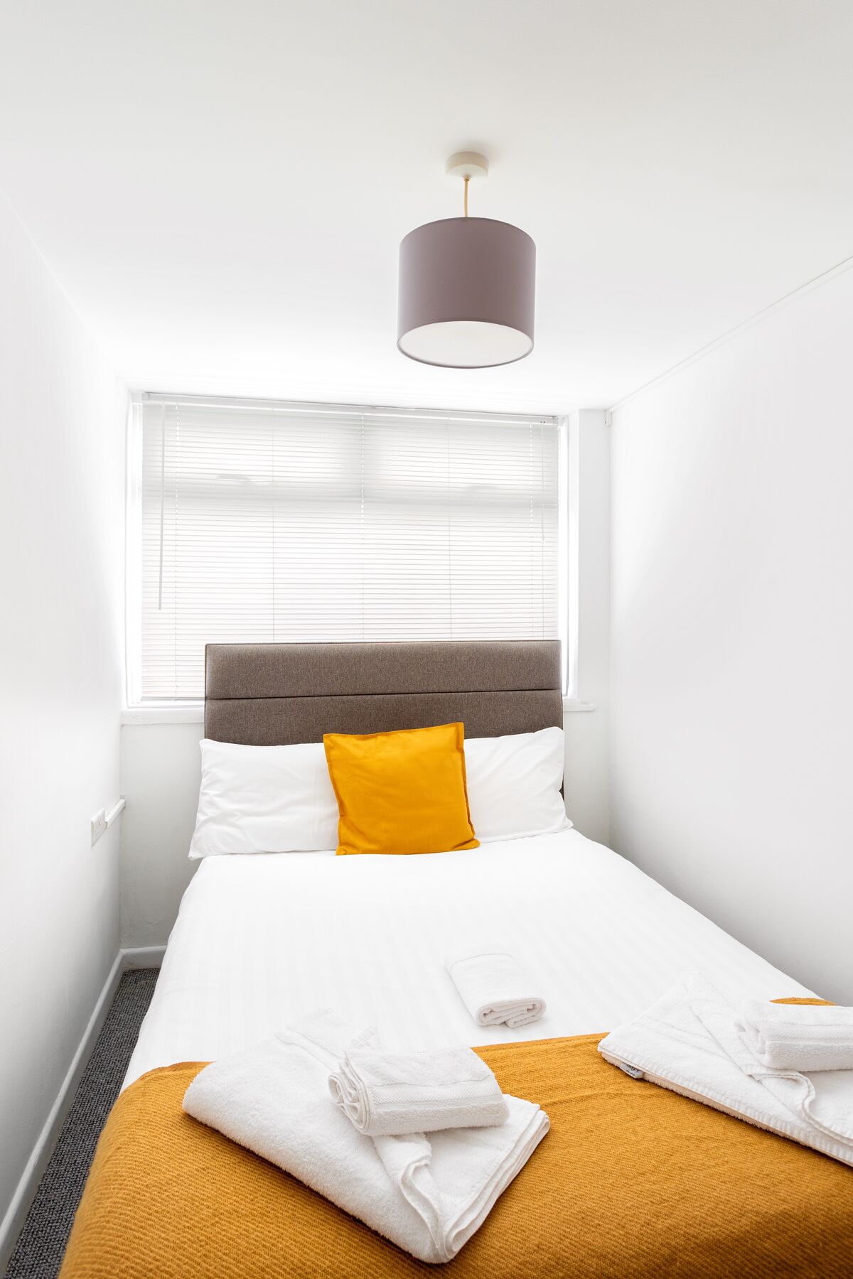 A neatly made bed with white and yellow bedding, a grey headboard, and a single white pillow.