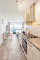 Una cocina moderna con horno empotrado, comedor con mesa y sillas, y vista al mar a través de amplias ventanas.