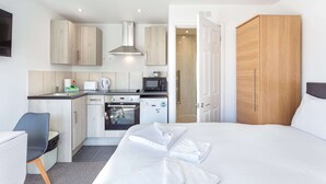 A hotel room with a bed, a small kitchenette, a microwave, a refrigerator, and a wooden wardrobe. - North Devon Resort (Ilfracombe)