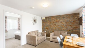 A room with two sofas, a dining table with plates and cutlery, a brick wall, and a ceiling light. - North Devon Resort (Ilfracombe)
