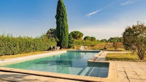 Une piscine rectangulaire, bordée d’une terrasse carrelée et entourée de verdure et d’arbres.