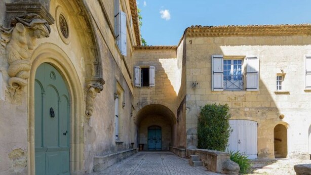 Une étroite ruelle pavée, située entre deux bâtiments dotés d’entrées en arc de cercle et d’une porte verte.