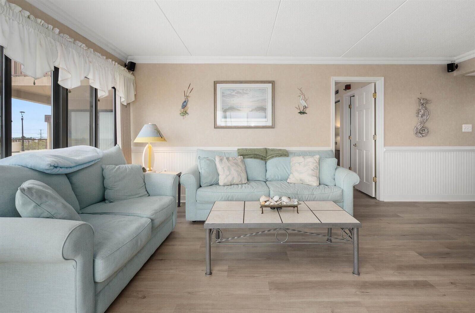 A living room with two light blue sofas, a coffee table with decorative items, a framed painting, and wall-mounted decorations.
