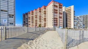 A beachfront hotel with multiple high-rise buildings, a sandy walkway, and a wooden fence.