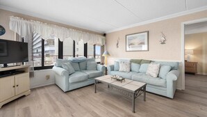 A living room with two light blue sofas, a coffee table, a TV on a stand, and a view of the outside balcony.