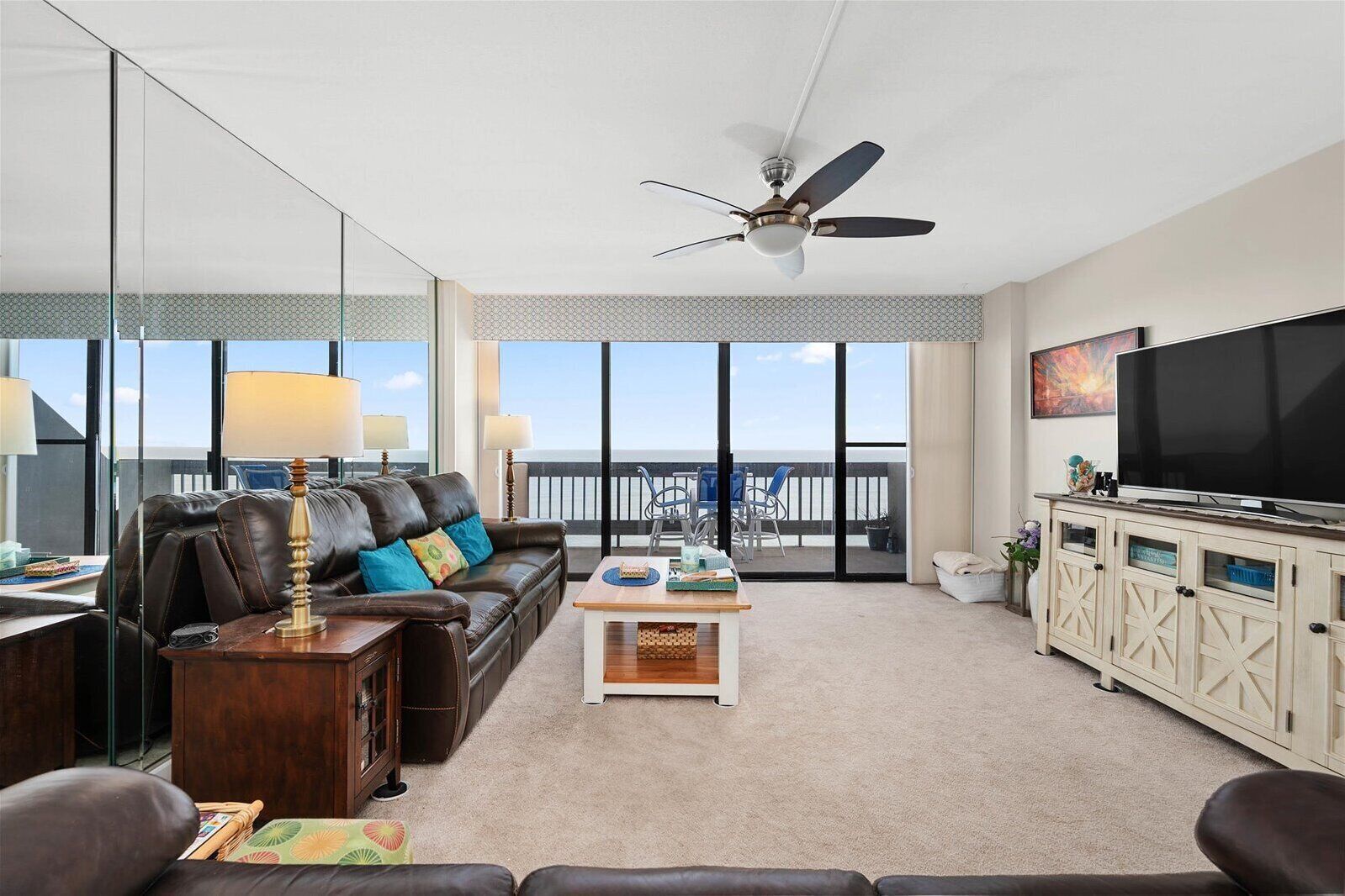 A living room with a leather sofa, a coffee table, a TV, and a balcony with a view.