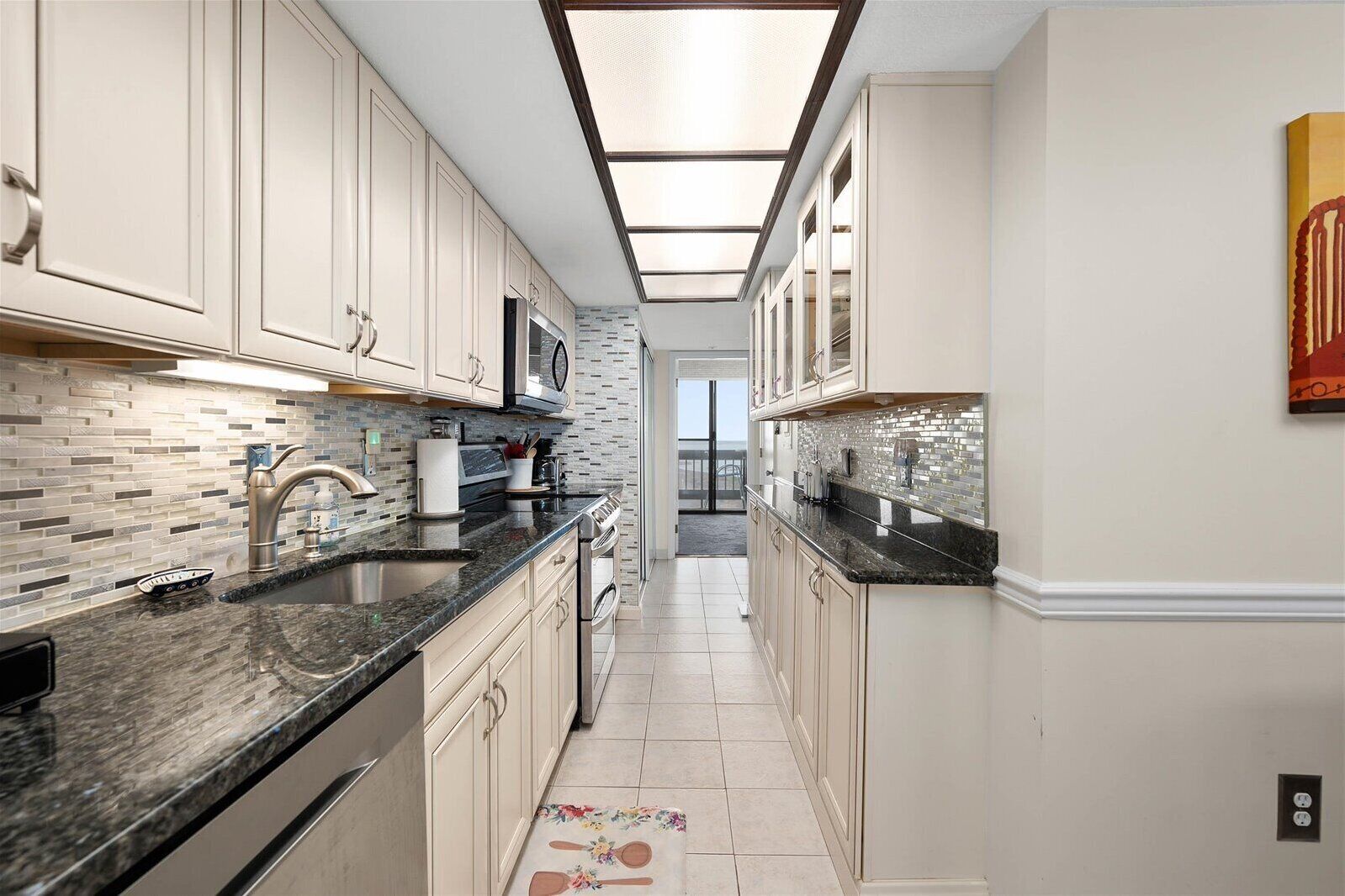 A modern kitchen with white cabinets, black countertops, and a skylight.