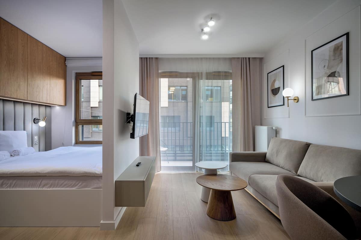 A modern hotel room with a bed, a sofa, a coffee table, and a TV.
