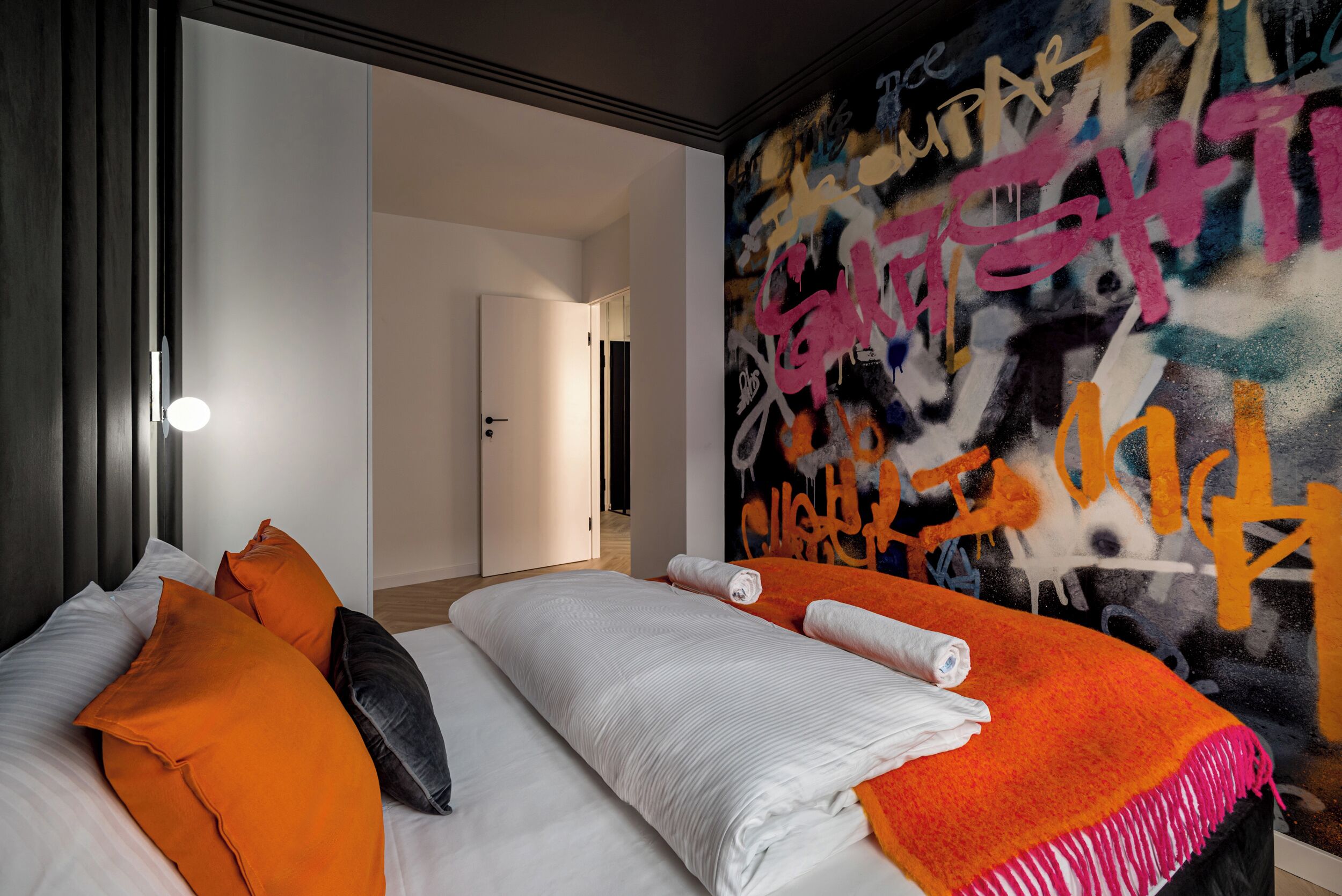 Une chambre d’hôtel avec un lit, des oreillers, une couverture et un mur couvert de graffitis.