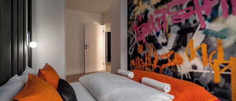 Une chambre d’hôtel avec un lit, des oreillers, une couverture et un mur couvert de graffitis.