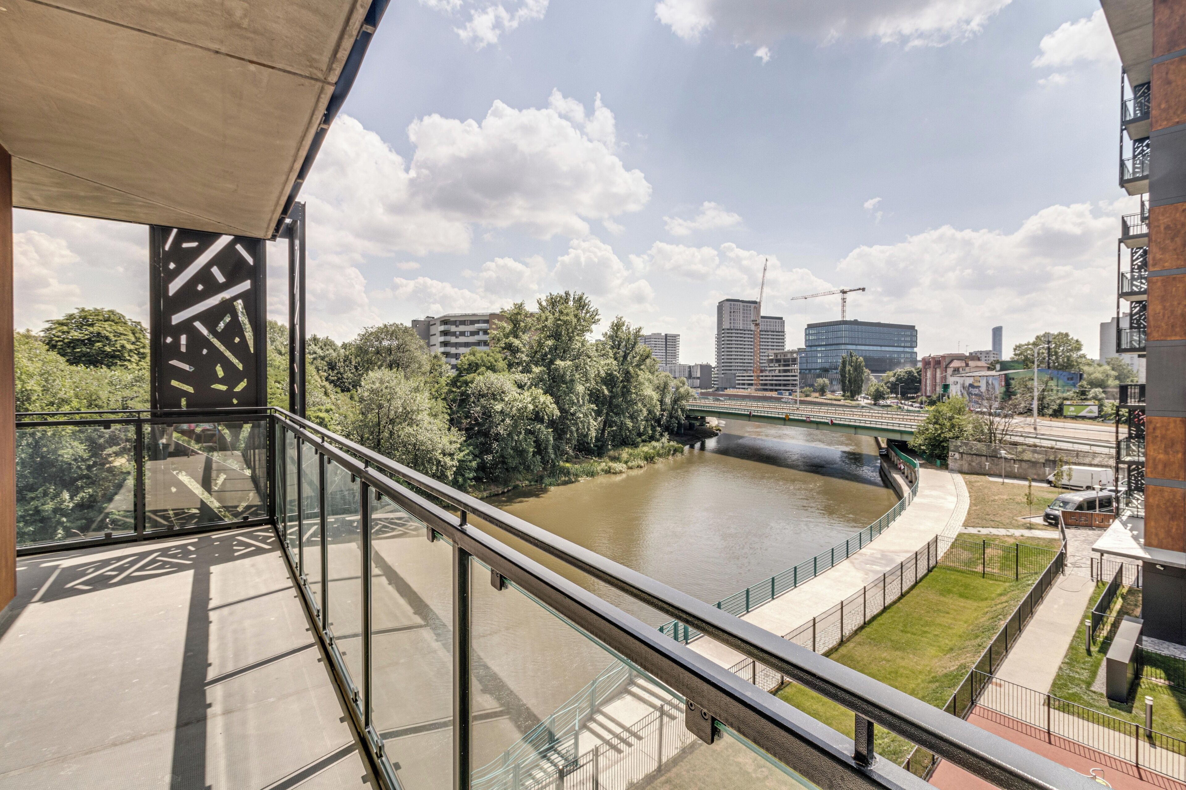 Een modern gebouw met een glazen balkon met uitzicht op een rivier, een brug en een stadsgezicht.