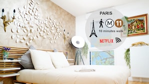 A modern bedroom with a bed, bedside tables, a wall-mounted lamp, and a view of the outdoors.