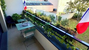 A balcony with a table and chairs, a French flag, and a view of neighboring buildings.