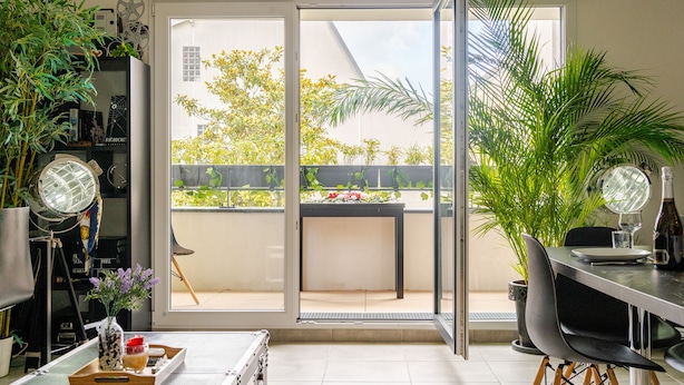 A modern living room with a sliding glass door leading to a balcony, a dining area with a table and chairs, and a variety of plants and decorative items.