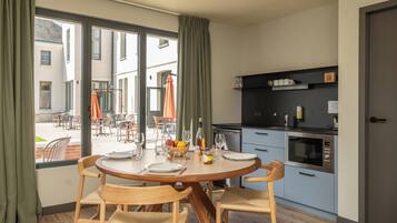 Un coin repas avec une table ronde dressée pour quatre personnes, des chaises en bois et une vue sur l’espace extérieur aménagé, visible à travers de grandes fenêtres.