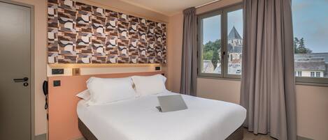 Quarto de hotel com cama, parede estampada, janela com cortinas e vista para um edifício.