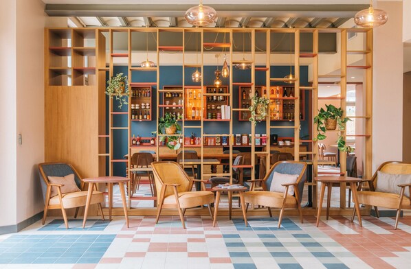 A cozy seating area with wooden chairs and tables, a bookshelf with various items, and hanging pendant lights.