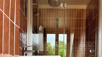 Un baño con ducha, lavamanos y vistas a árboles a través de una ventana.