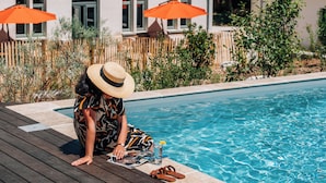Zona de piscina con cubierta de madera, piscina y dos sombrillas naranjas.
